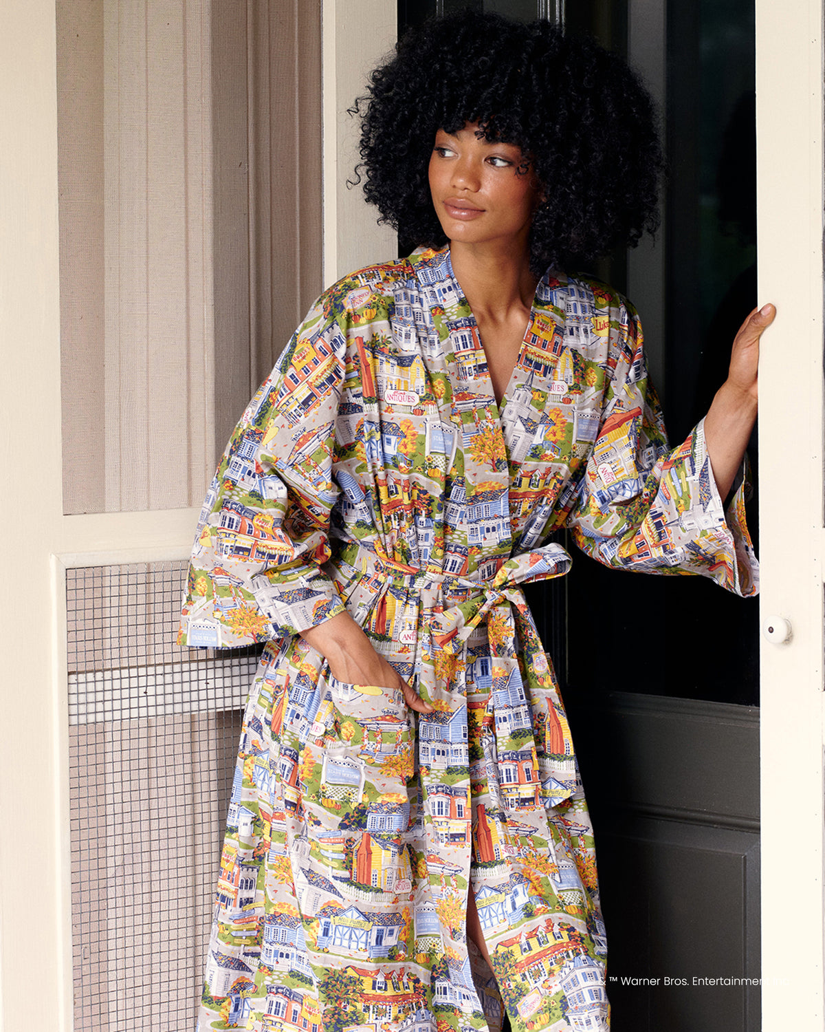 Person wearing the full-length Stars Hollow robe with wide sleeves, sash belt, and illustrated town print.