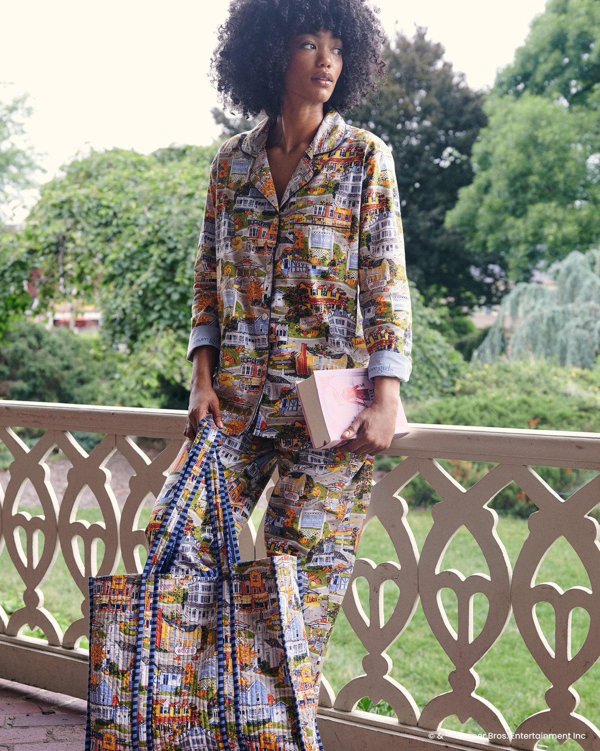 Stars Hollow printed traveler tote held by a model on a balcony, with the illustrated town pattern visible.