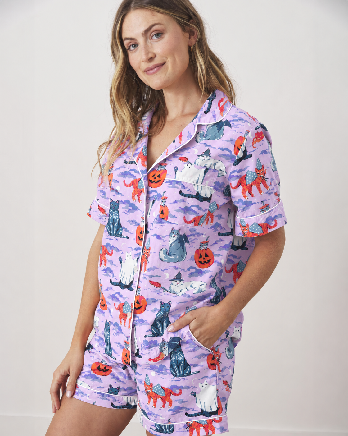 Three-quarter view of the lavender Halloween House Cats pajama top and shorts, showing the collar, chest pocket, buttons, and printed cats and pumpkins.