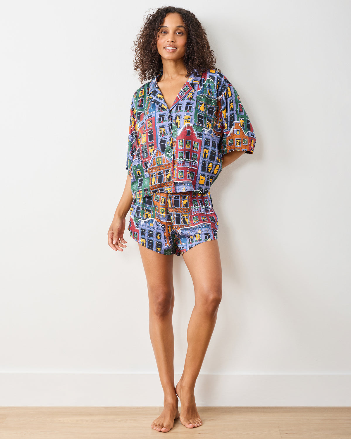Full-length front view of a person wearing the Manhattan Christmas cropped top and matching shorts set with a colorful brownstone holiday print.