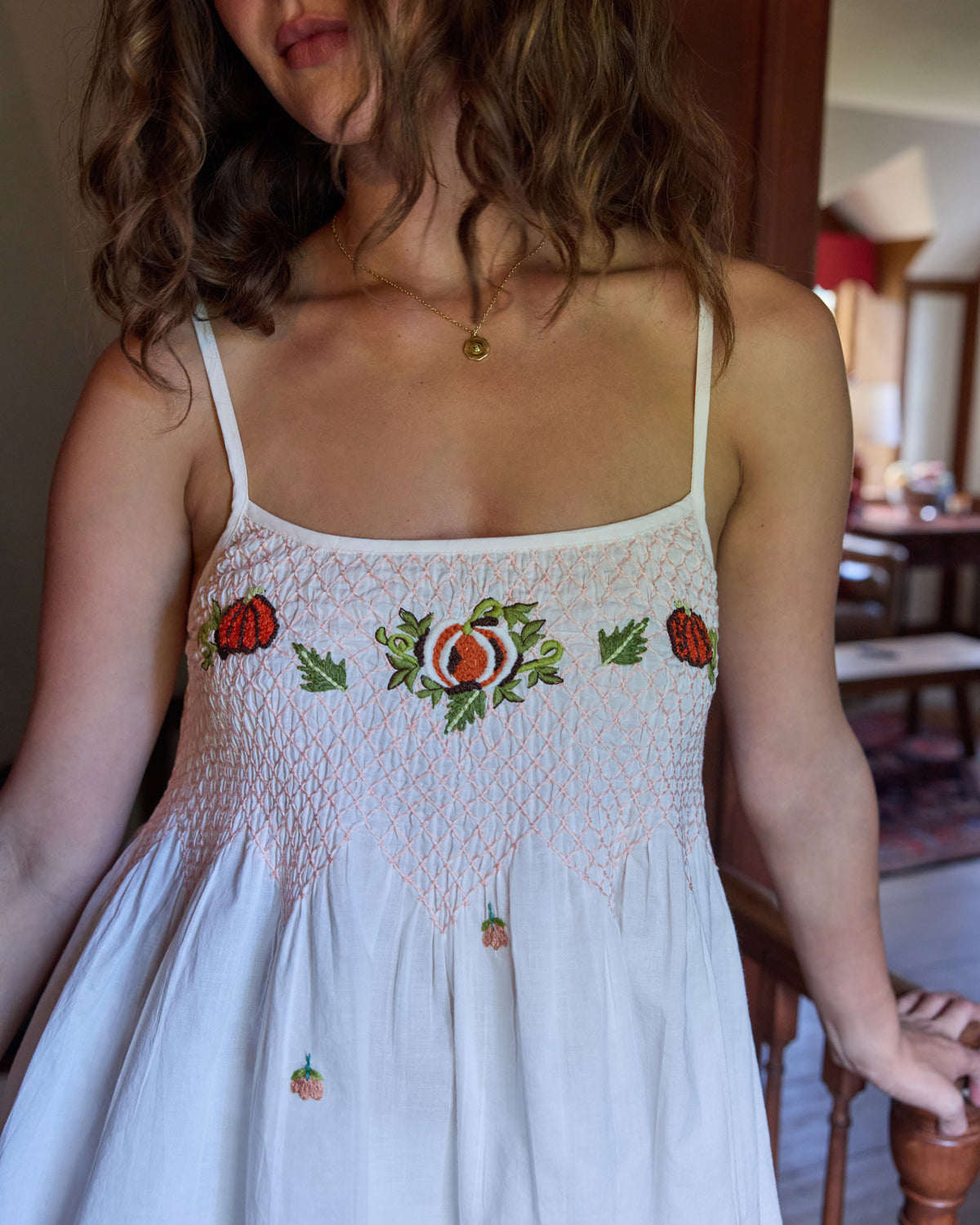 Close-up of the camisole top showing smocked stitching, thin straps, and embroidered pumpkin motifs across the chest and skirt.