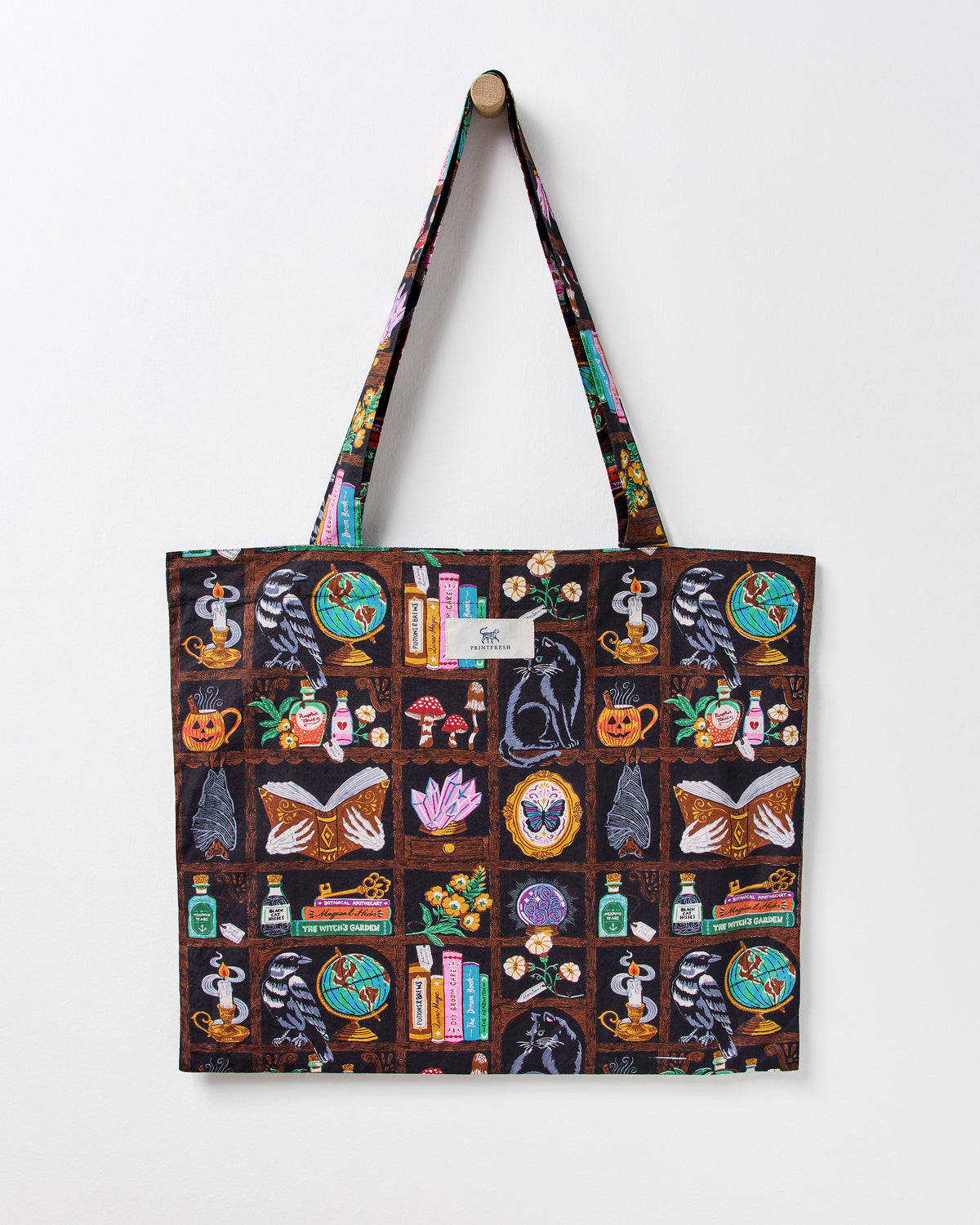Enchanted Study tote bag with long handles and a dark illustrated print of ravens, globes, books, bottles, candles, cats, and other motifs.