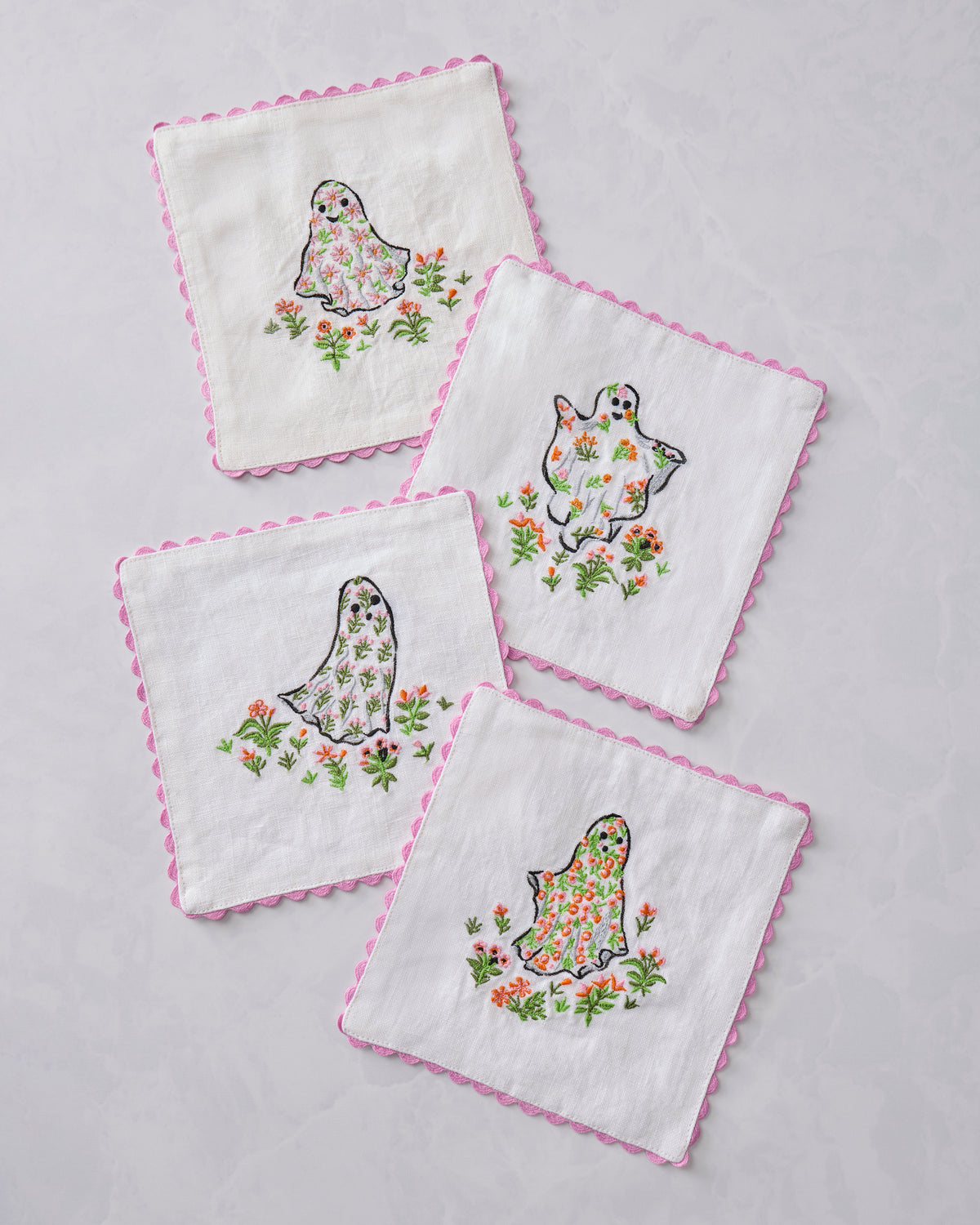 Four Gardening Ghosts cocktail napkins arranged at angles, each with a floral embroidered ghost design and pink scalloped edges