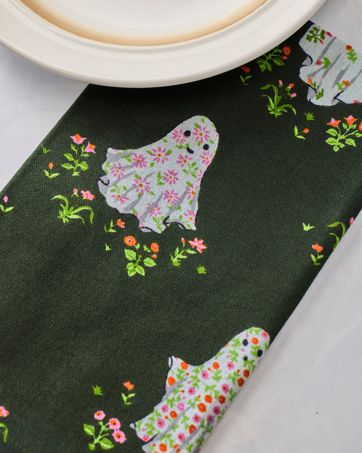 Close-up of a dark green dinner napkin printed with a floral ghost beneath a plate.