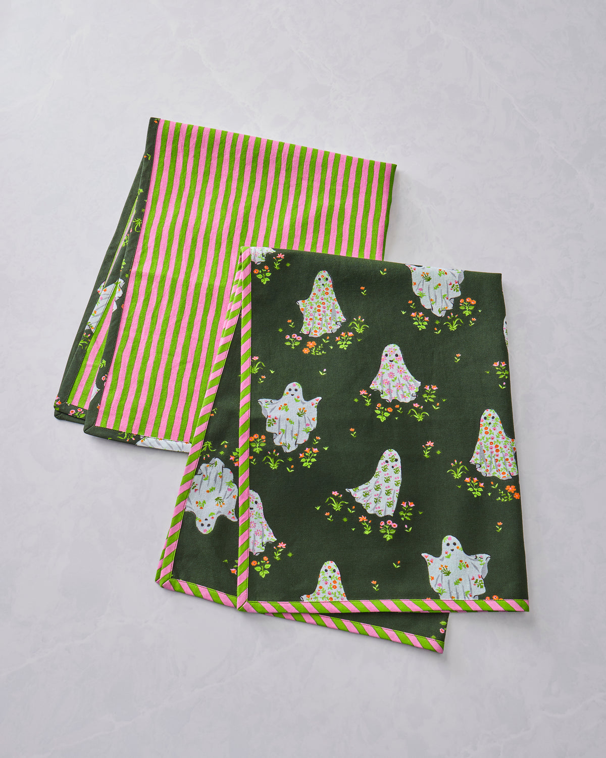 Two tea towels showing a dark green ghost-and-flower print and a pink-and-green striped reverse side.