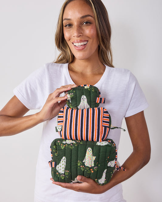 Person holding three quilted pouches in different sizes, with ghost-and-garden prints and a striped middle pouch.