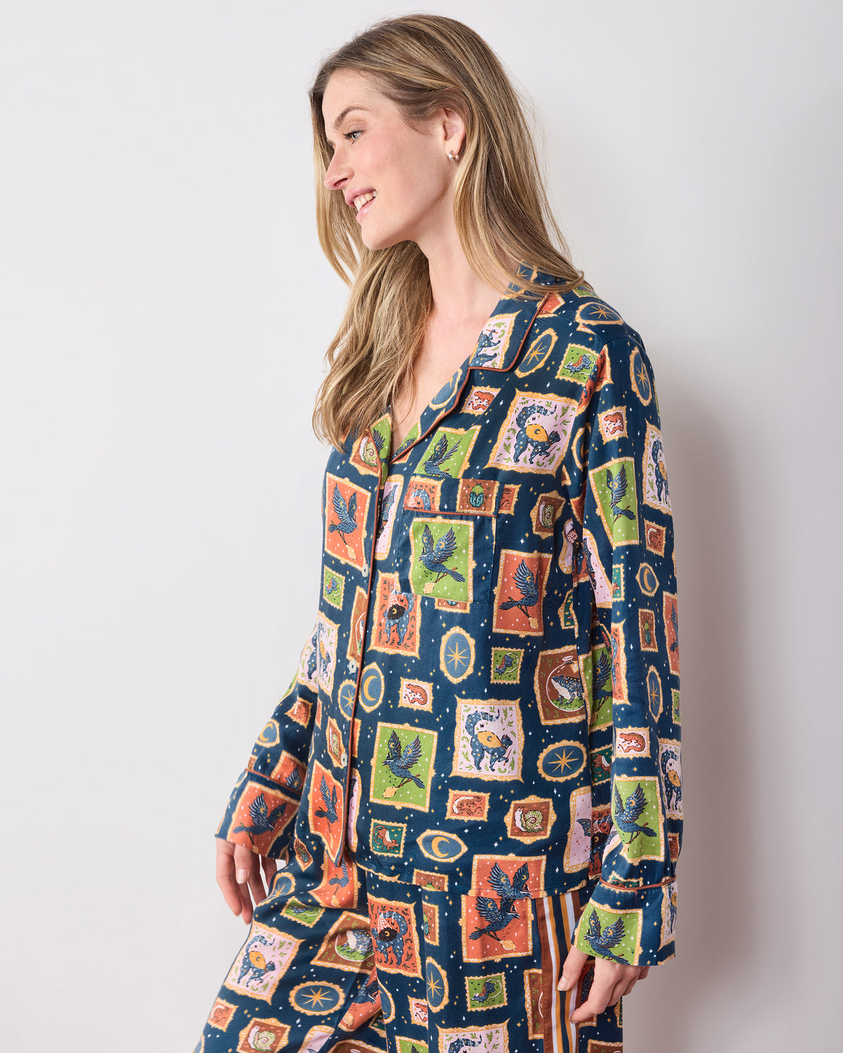 Three-quarter side view of the Midnight Gallery Night Sky pajama top showing its collar, buttons, long sleeves, chest pocket, and patterned print.