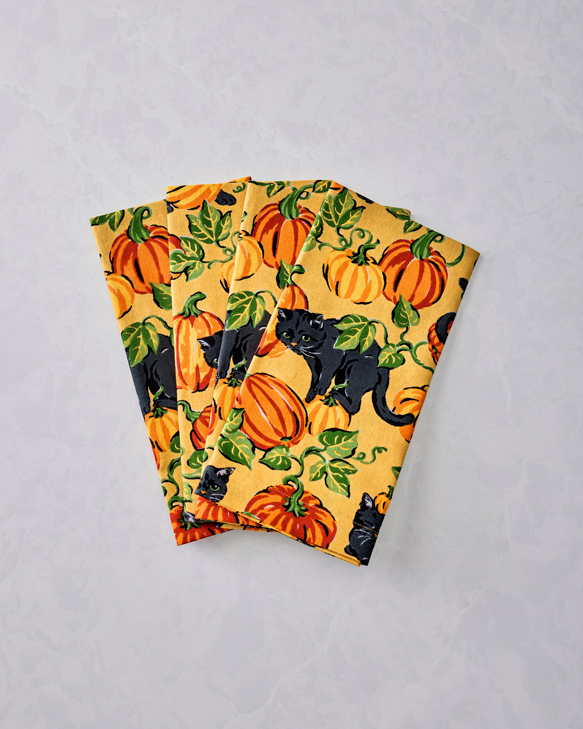 Folded dinner napkins with an orange background pattern of pumpkins, green leaves, and black cats.