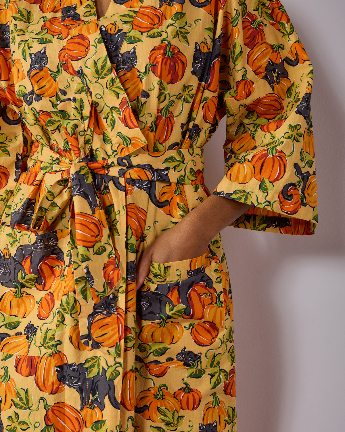 Close-up of the Pumpkin Prowl long robe showing its tied belt, sleeve, and deep pocket in a pumpkin and black-cat print.