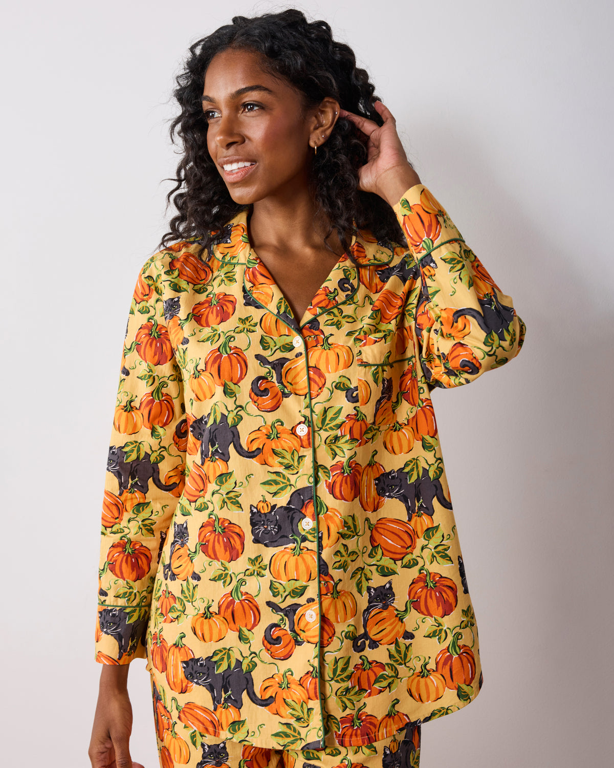 Close view of a long-sleeve button-down pajama top with pumpkin and black cat print, piping, and front buttons.