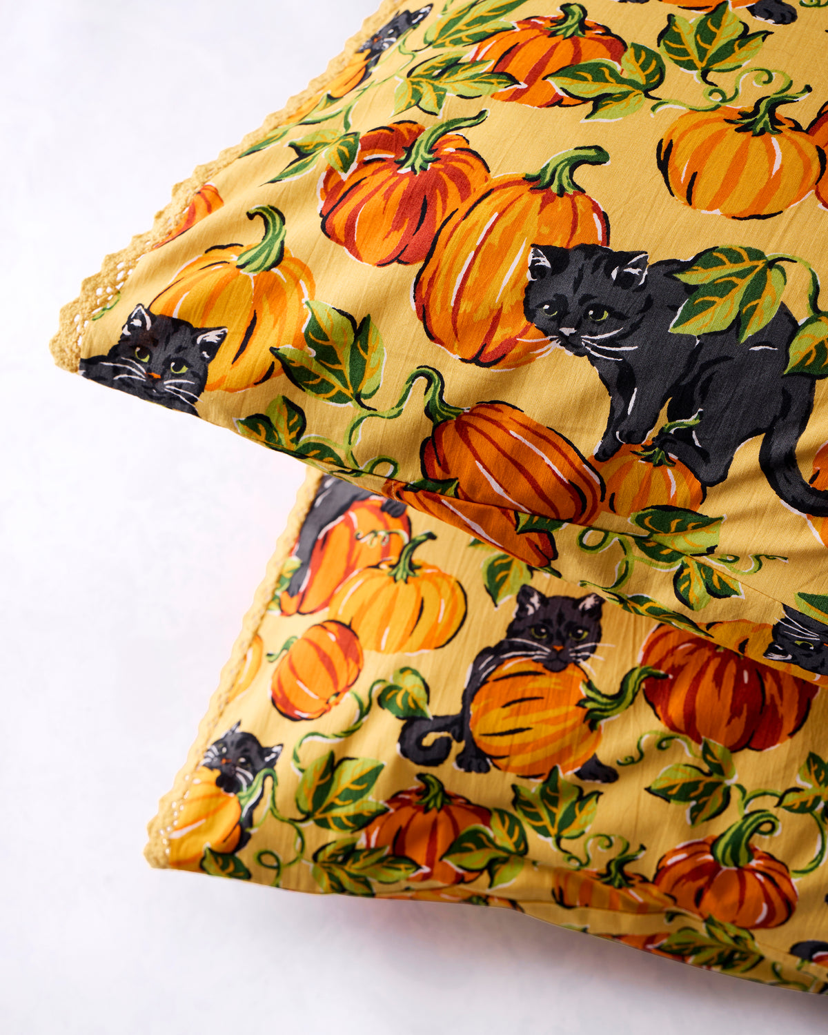 Two Pumpkin Prowl pillowcases layered together, showing black cats and pumpkins across the print and lace trim along the edges.