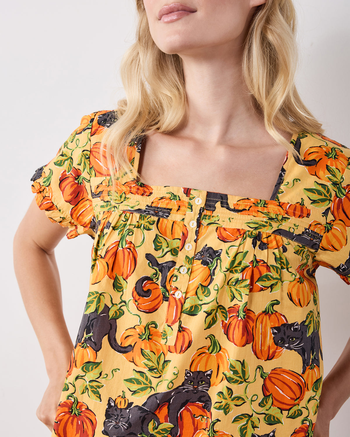 Close-up of the Pumpkin Prowl cropped pajama top showing its pintuck neckline, button front, ruffled sleeves, and pumpkin-and-black-cat print.