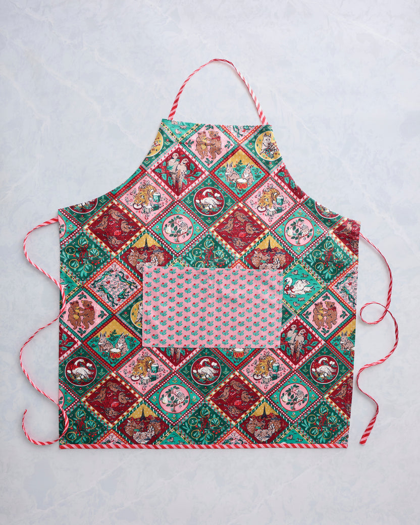 Flat lay of a Christmas-patterned apron with a pink floral pocket and red-and-white trim.