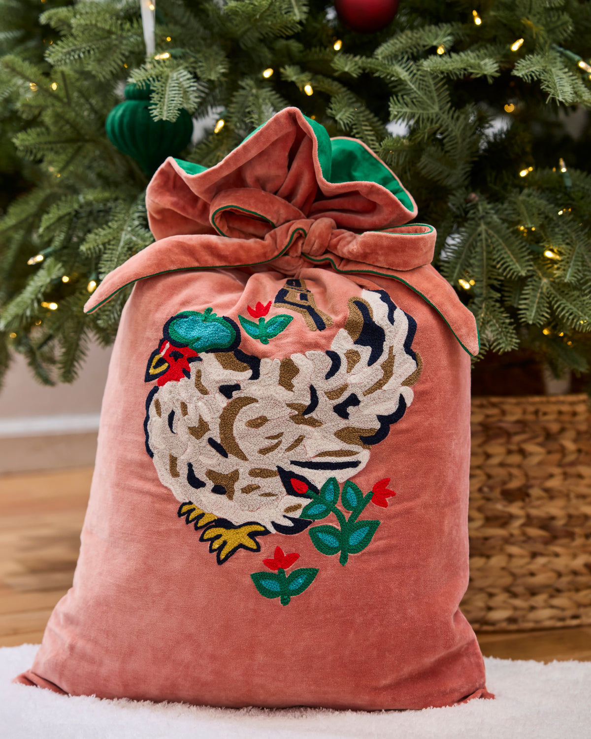Embroidered gift sack with a tied top and a white hen design, placed in front of a decorated Christmas tree.