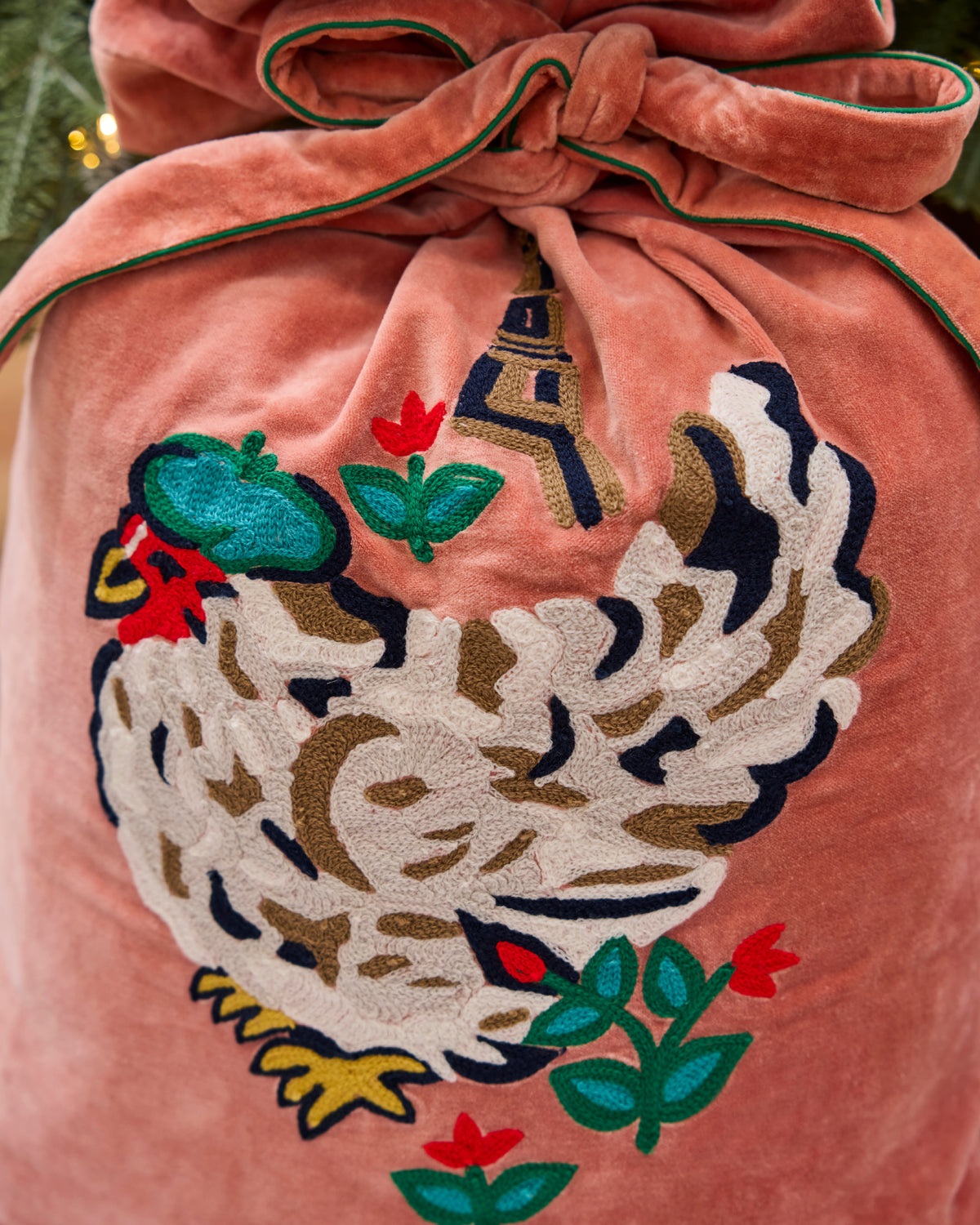 Close-up of a pink velvet gift sack with embroidered French hens, flowers, and a coordinating tie.