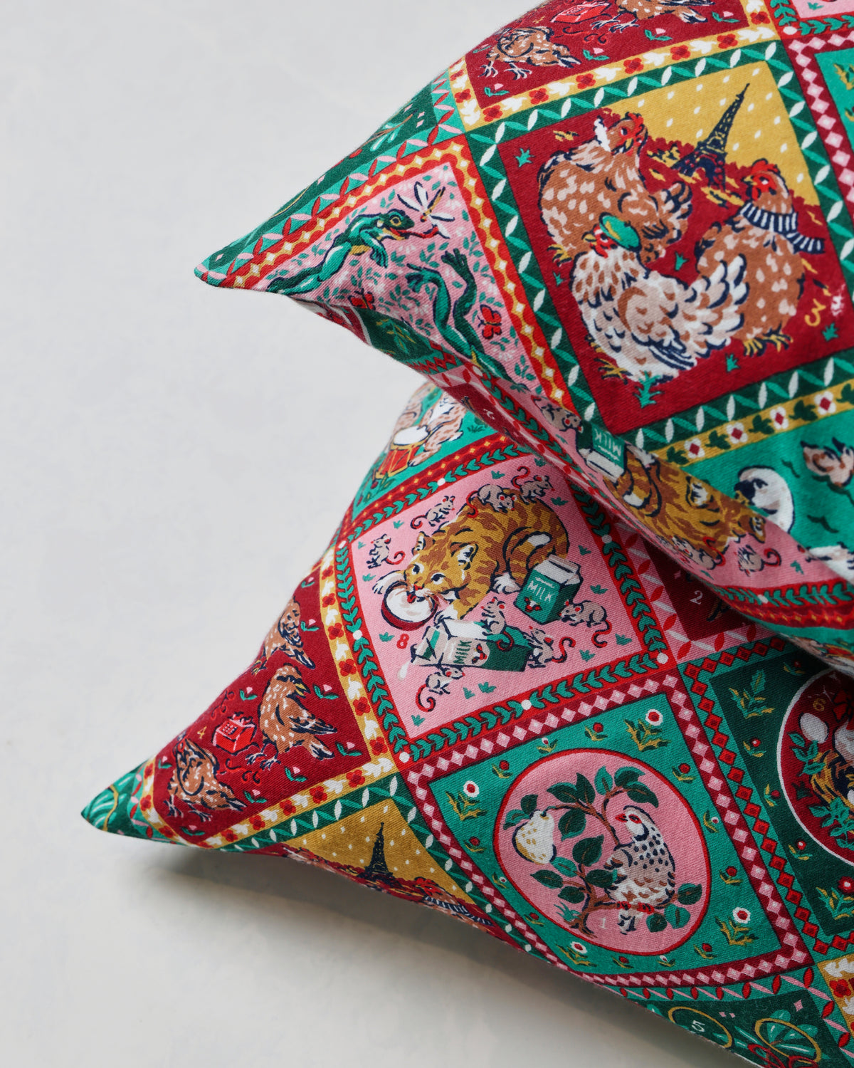 Close-up of overlapping Christmas-themed pillowcases showing colorful diamond-patterned illustrations of animals and holiday scenes.