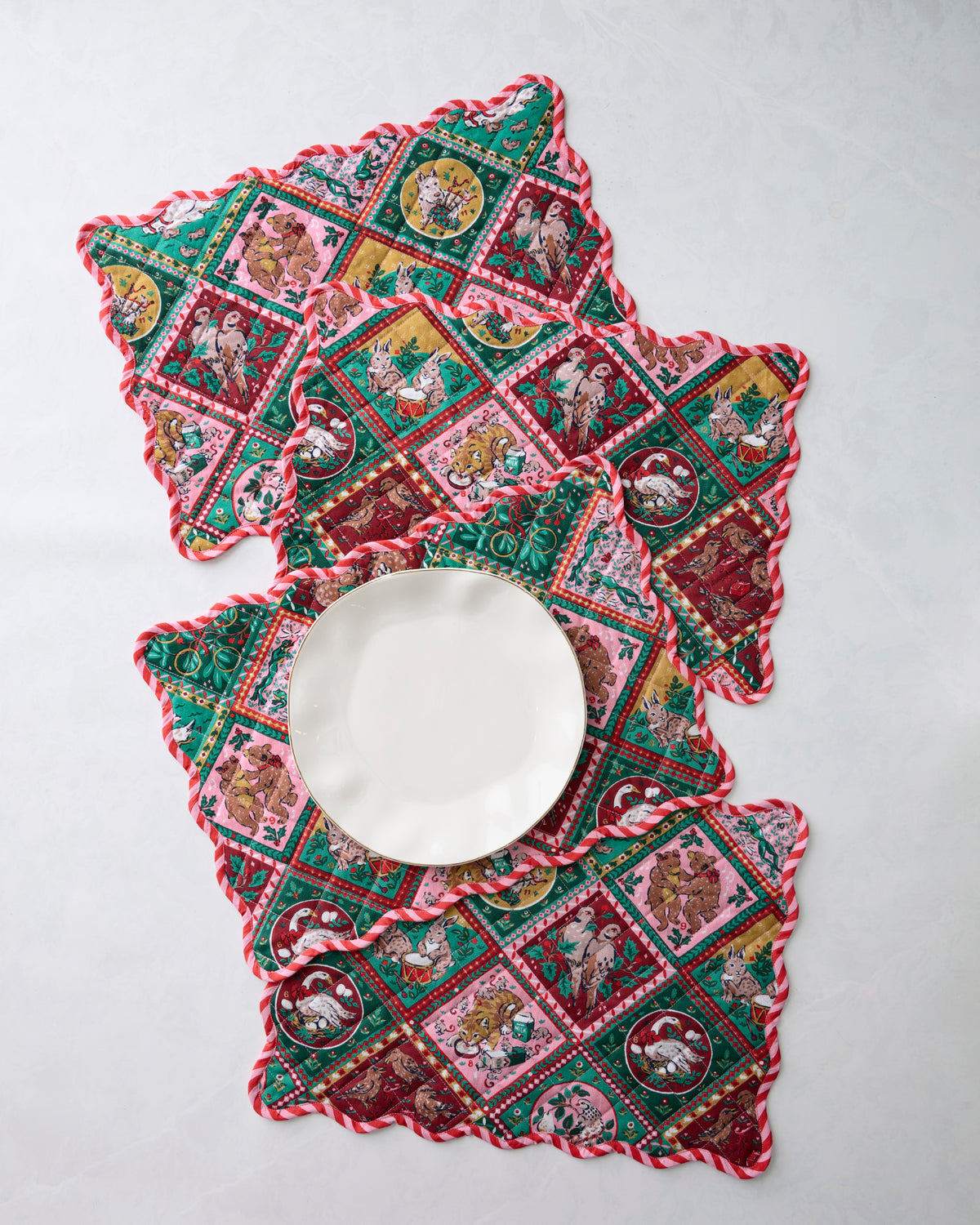 Four Christmas-patterned placemats arranged around a white plate, showing their scalloped edges.