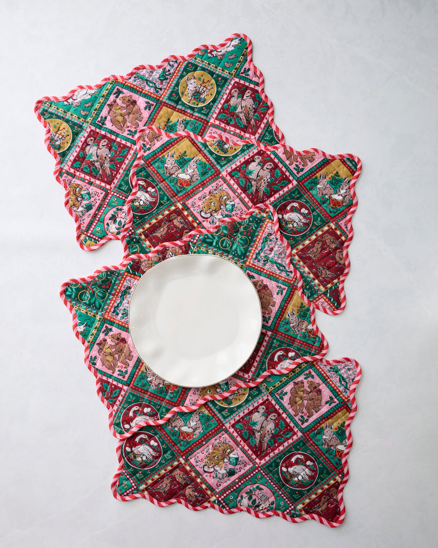 Four Christmas-patterned placemats arranged around a white plate, showing their scalloped edges.