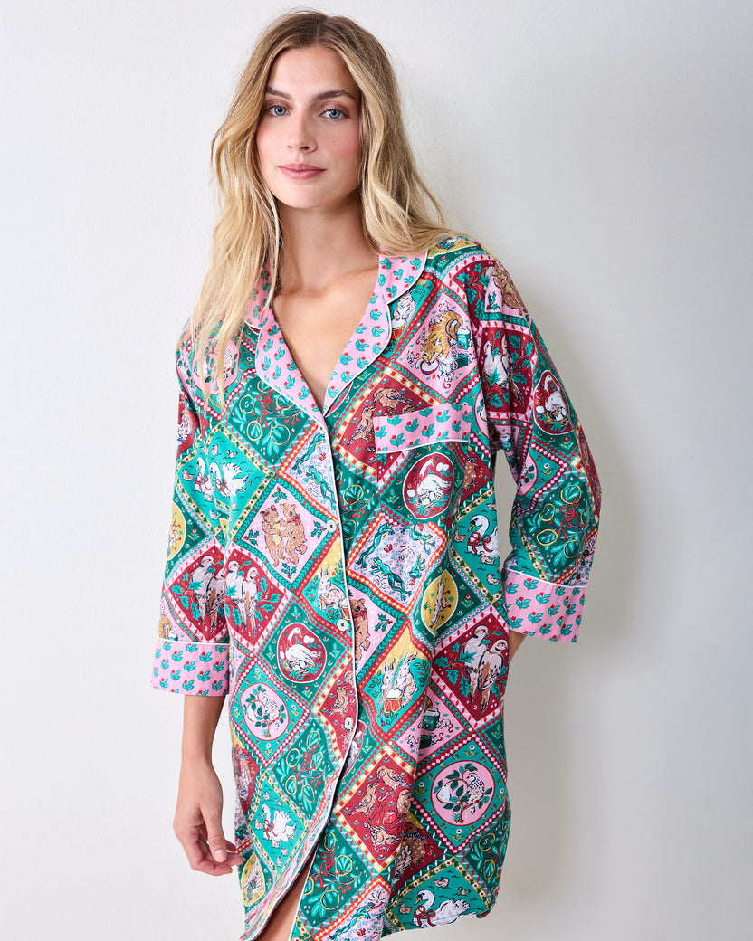 Person wearing a long button-front sleep shirt with a colorful patchwork print of Christmas and storybook vignettes.