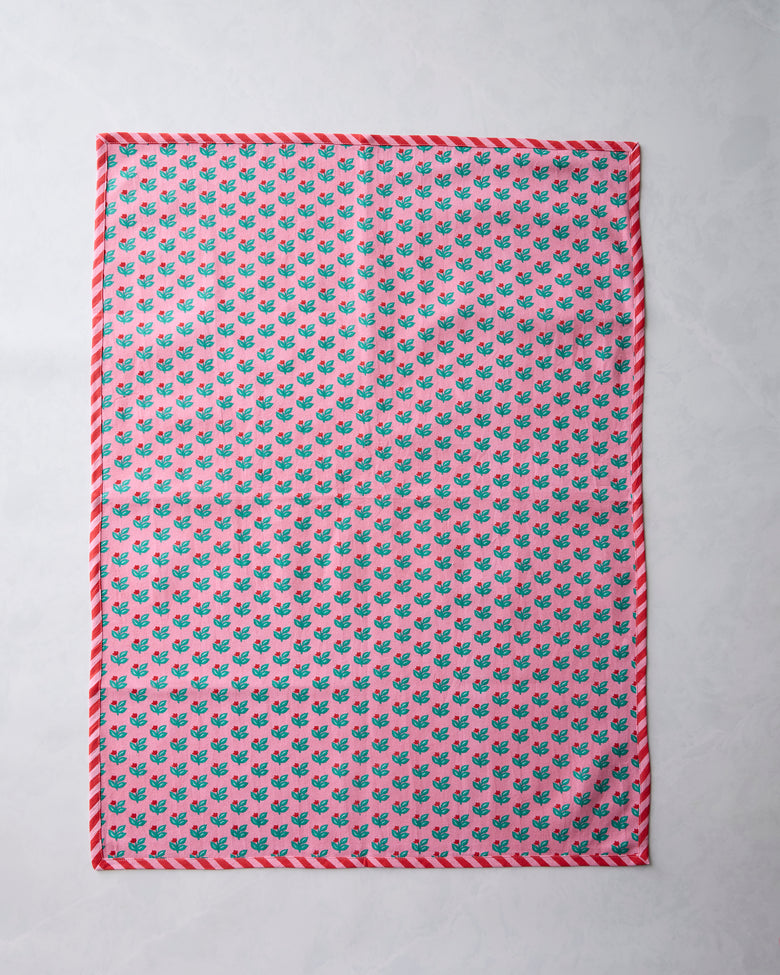 Flat lay of a pink tea towel with a repeated green leaf pattern and red-and-white trim.