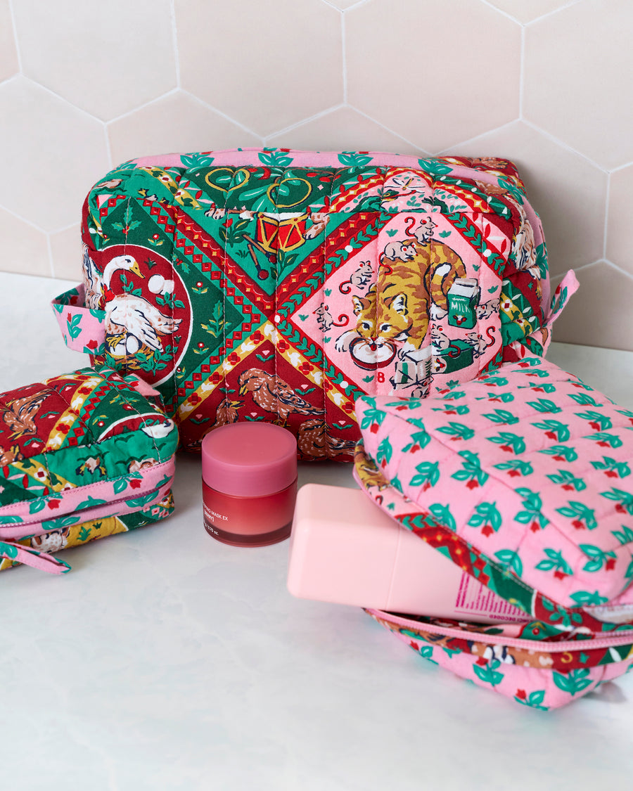 Three quilted 12 Days of Christmas pouches arranged with the largest pouch open, showing a red, green, and pink holiday print with birds, a cat, and festive scenes.