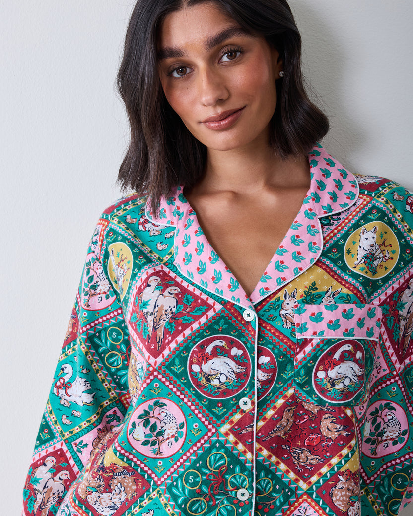 Close front view of a long-sleeved button-front pajama set with a multicolored holiday animal print, pink floral collar, and chest pocket.