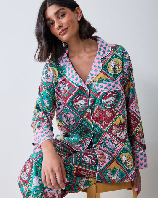 Person wearing a long button-front pajama set with a colorful patchwork print of Christmas and storybook vignettes.