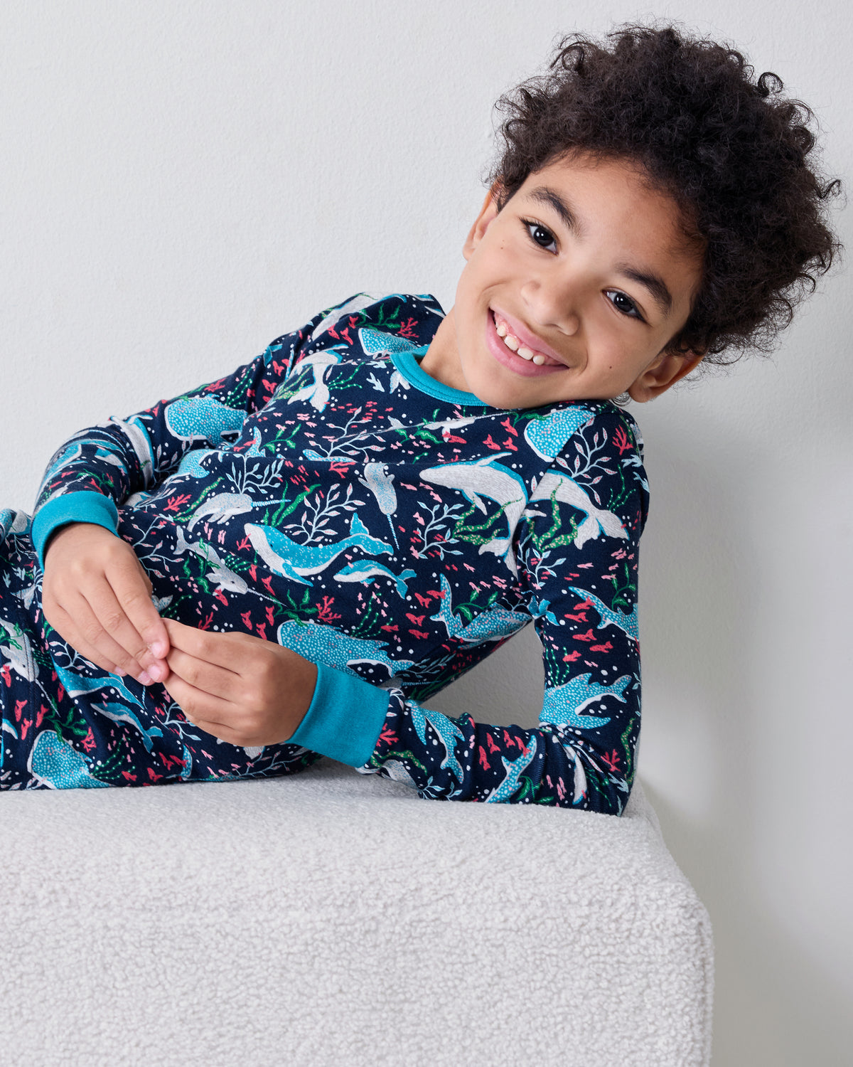 Close view of a child wearing the Arctic Sealife long-sleeve pajama top and pants while reclining on a white ottoman.