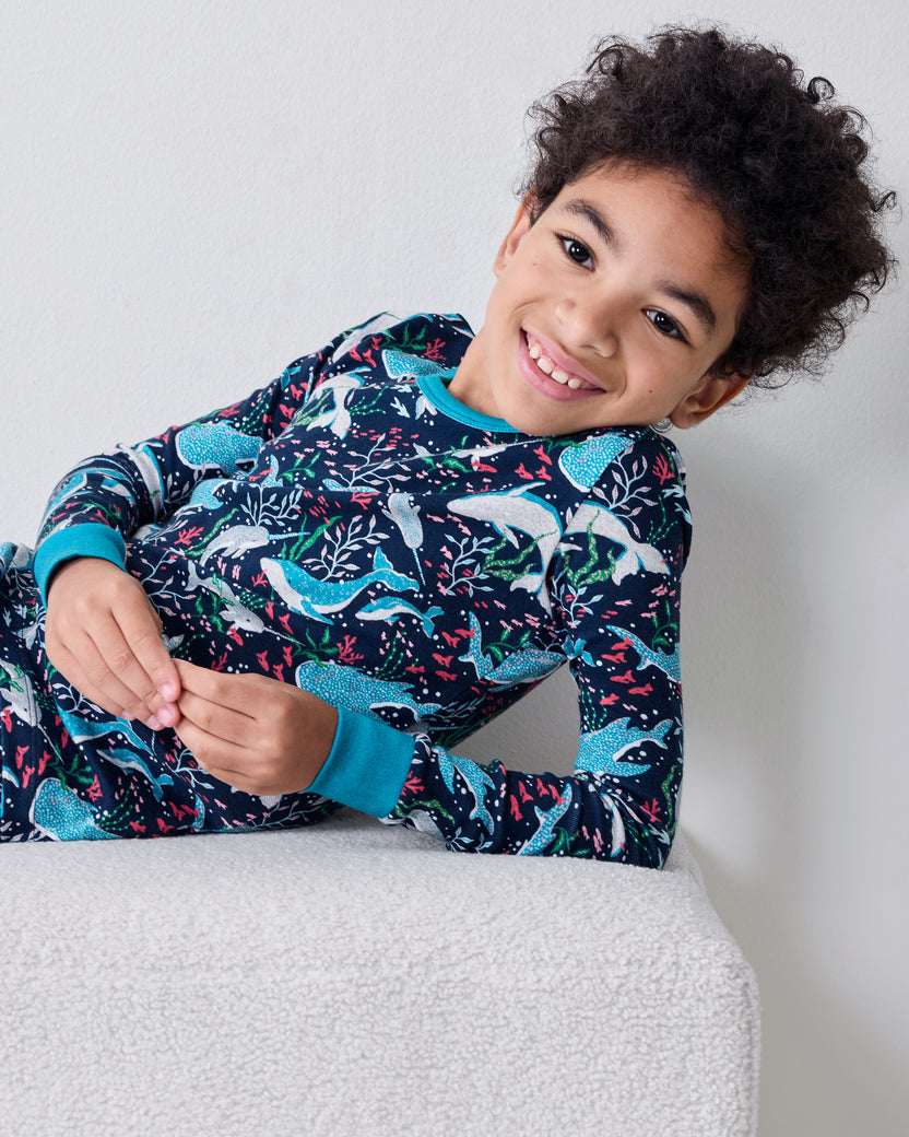 Close view of a child wearing the Arctic Sealife long-sleeve pajama top and pants while reclining on a white ottoman.