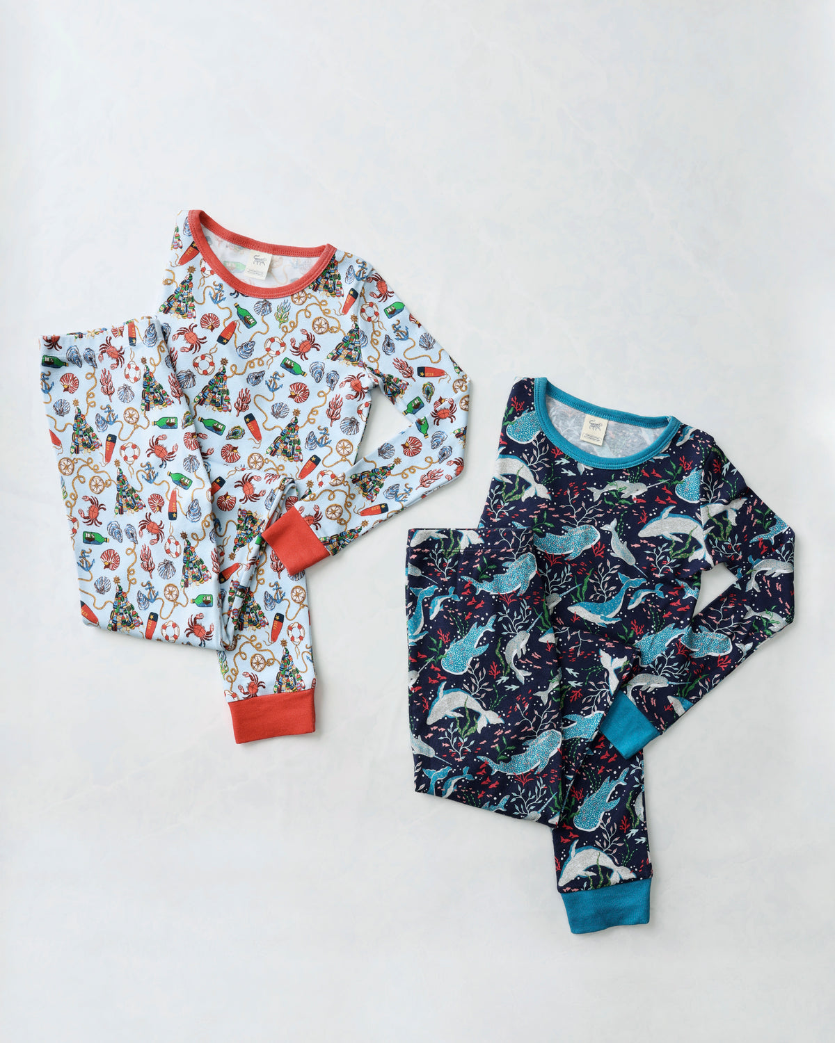 Flat lay of two children's long-sleeve pajama sets: a light nautical-print set and a dark Arctic Sealife set.