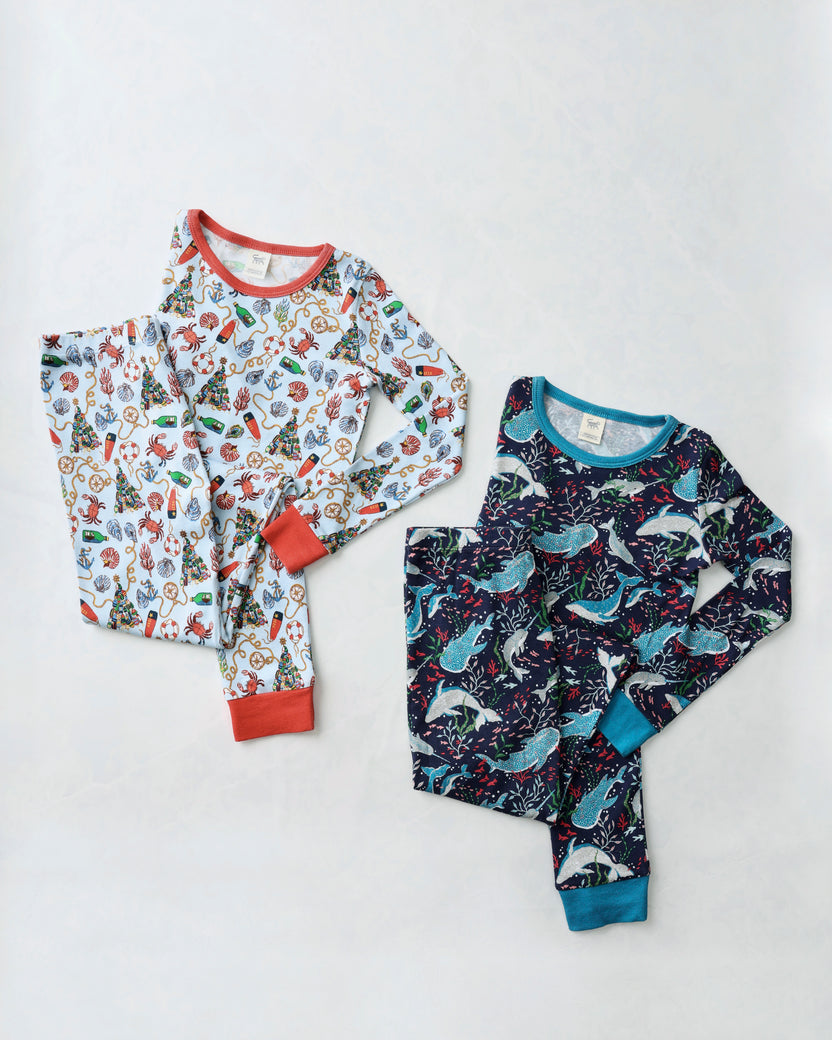 Flat lay of two children's long-sleeve pajama sets: a light nautical-print set and a dark Arctic Sealife set.