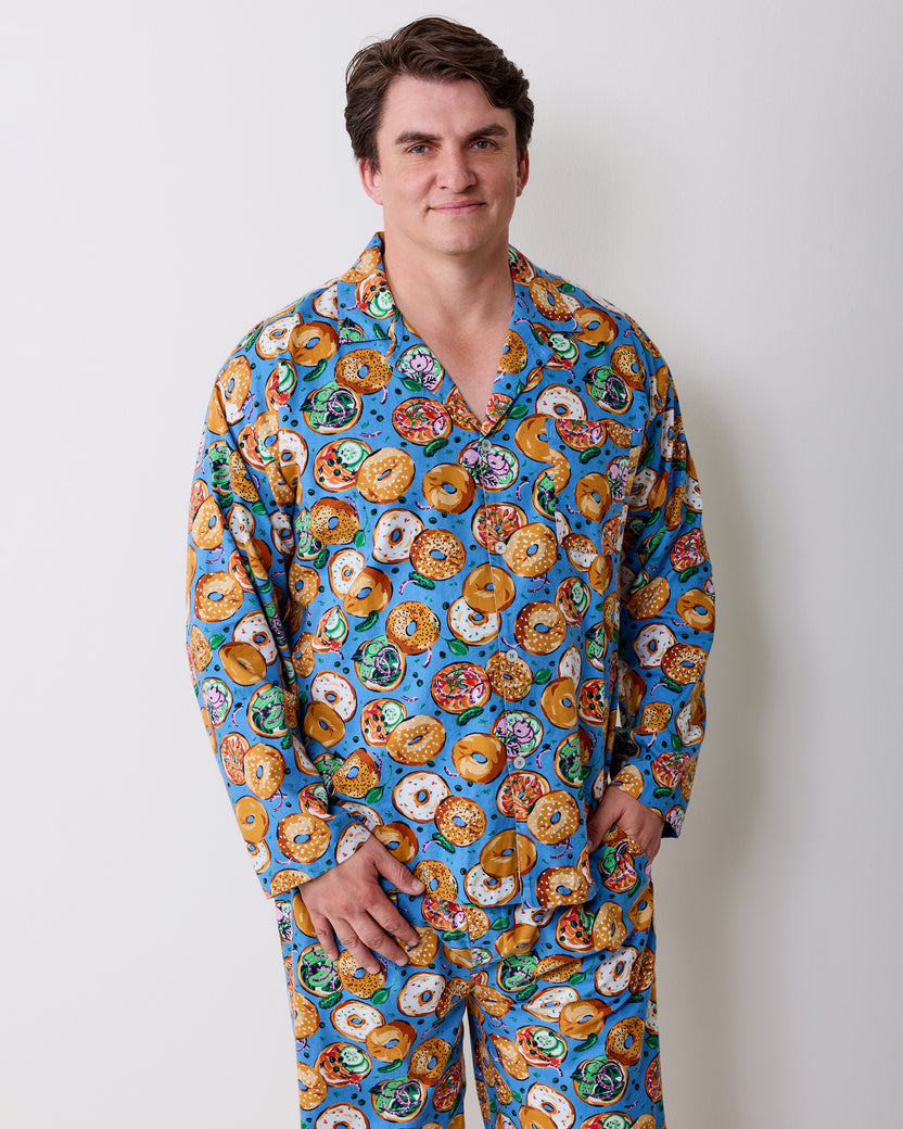Person wearing a blue long-sleeve button-front pajama top and matching pants with a bagel print.