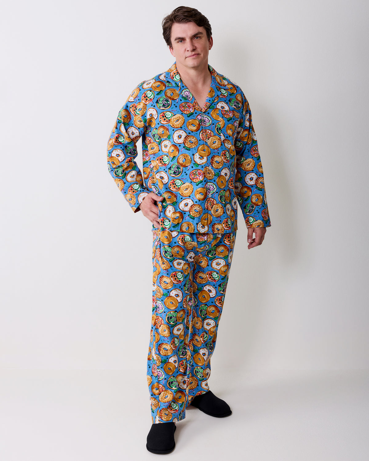 Full-length view of a person wearing a blue bagel-print long-sleeve pajama set with black slippers.