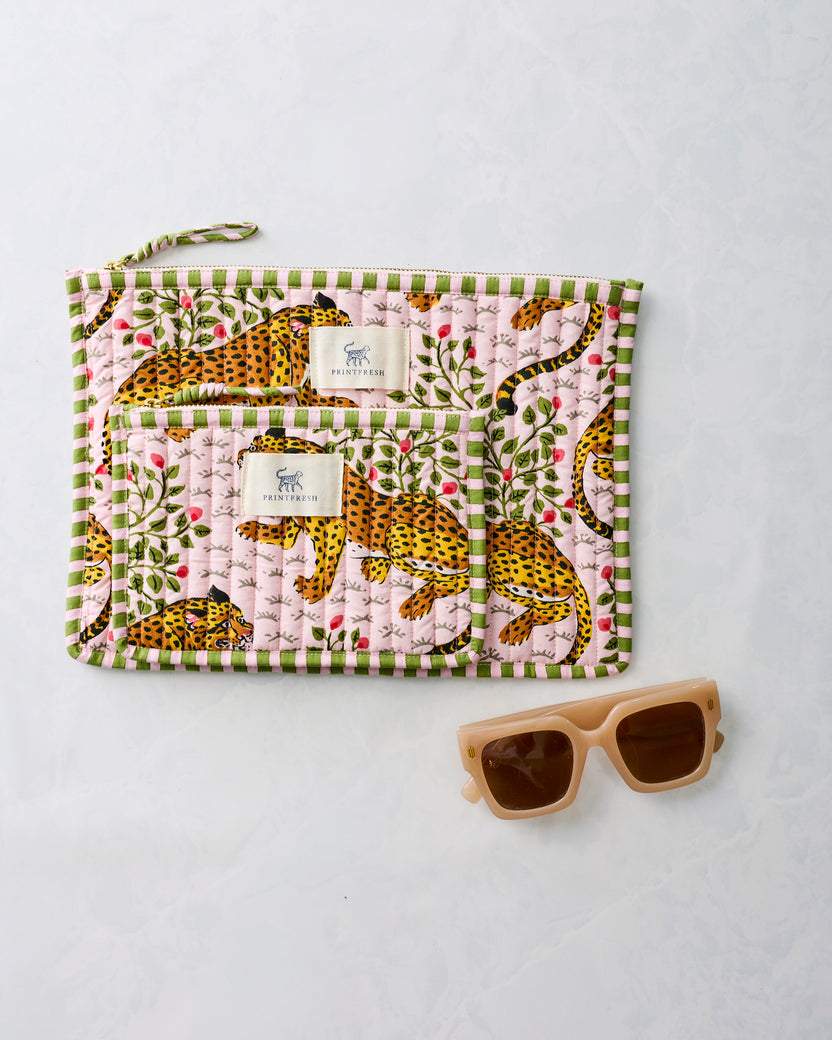 Two pink leopard-print zippered pouches displayed together beside sunglasses.