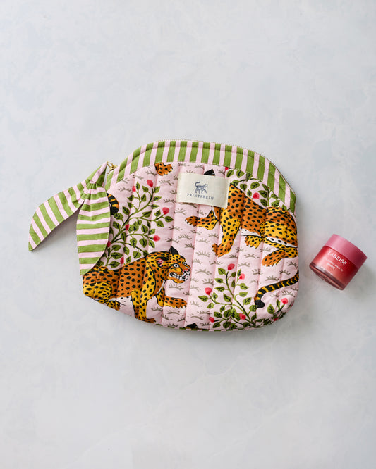 Pink quilted leopard-print makeup bag with green striped trim, shown beside a small cosmetic jar