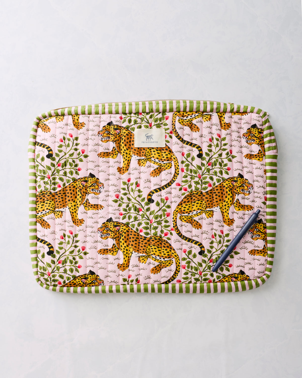 Pink leopard-print quilted laptop sleeve with green striped trim, shown with a pen on the front