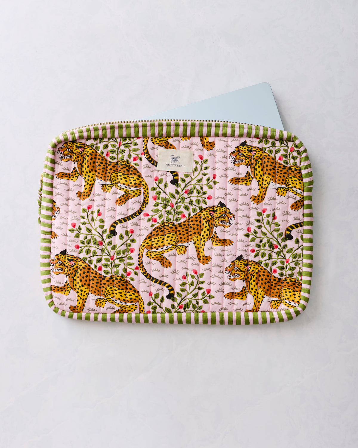 Quilted laptop sleeve with a leopard-and-floral print, green striped trim, and a laptop partly inserted at the top.