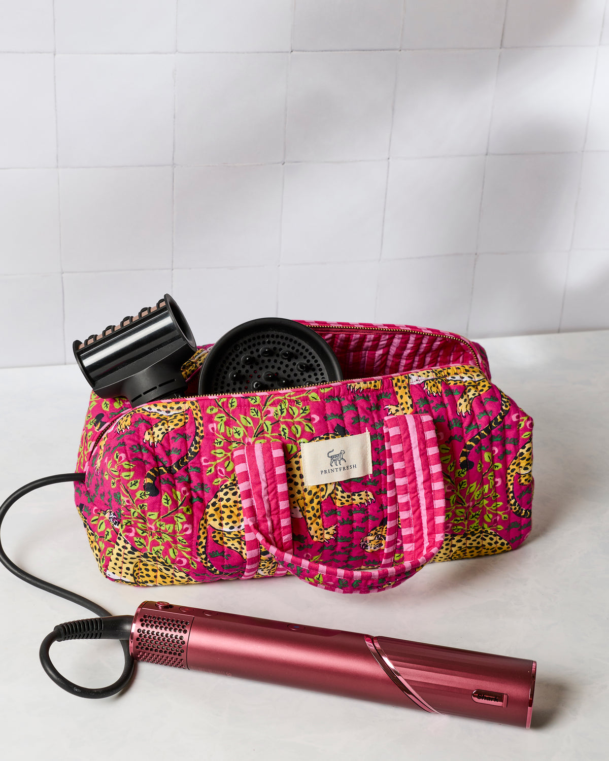Open hot pink quilted hair tool travel case with black styling attachments inside and a pink styling tool placed in front.