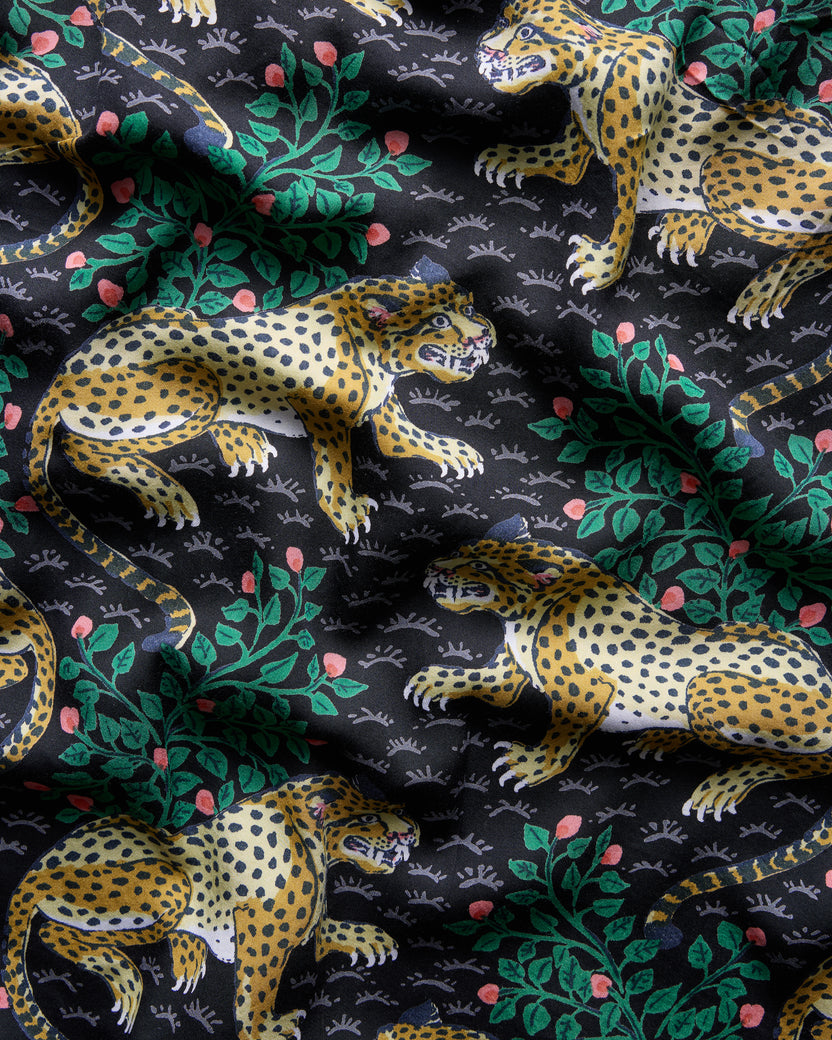 Close-up of the Bagheera dress print showing repeated leopards, leafy branches, and small pink flower shapes on a dark background.