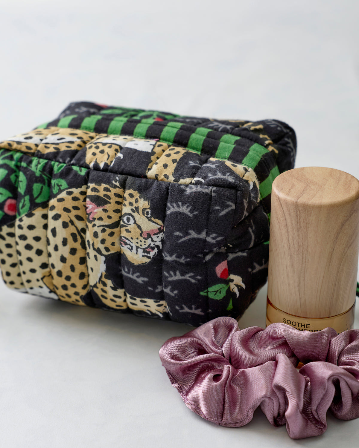 Bagheera Ink quilted essentials wristlet shown beside a wooden bottle and a mauve scrunchie.
