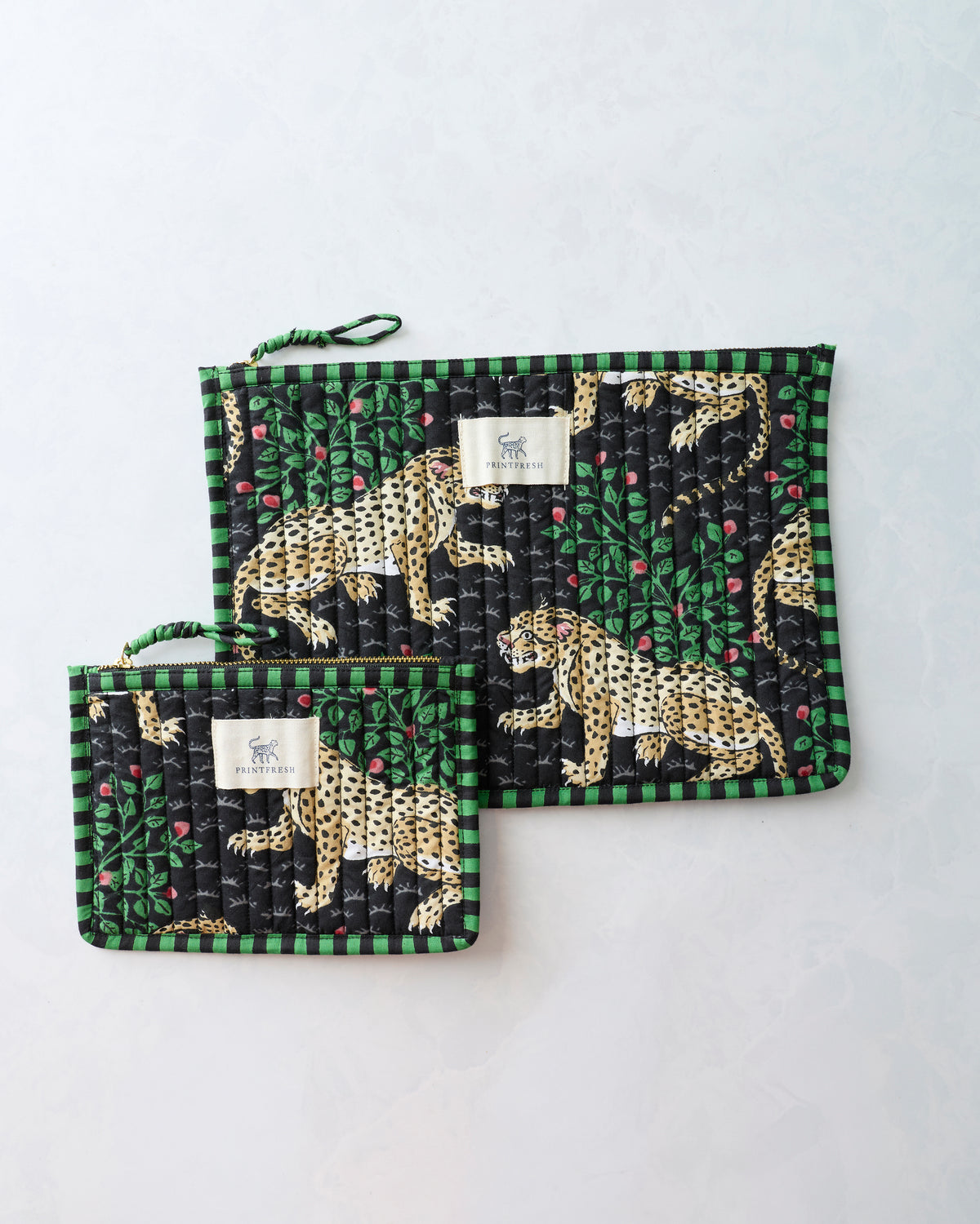 Large and small Bagheera Ink flat pouches with leopard-and-leaf print, zippers, wrist loops, and Printfresh labels.