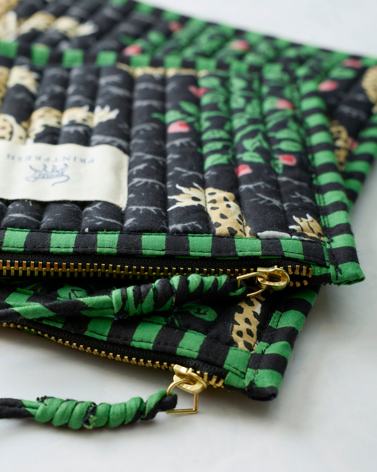 Close-up of Bagheera Ink flat pouch zippers, gold-toned pulls, and twisted fabric wrist loops.
