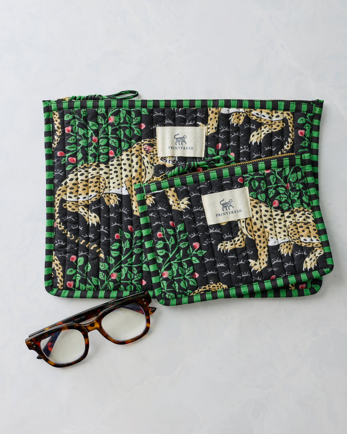 Bagheera Ink flat pouch duo with leopard-and-leaf print, shown with tortoiseshell eyeglasses and Printfresh labels.