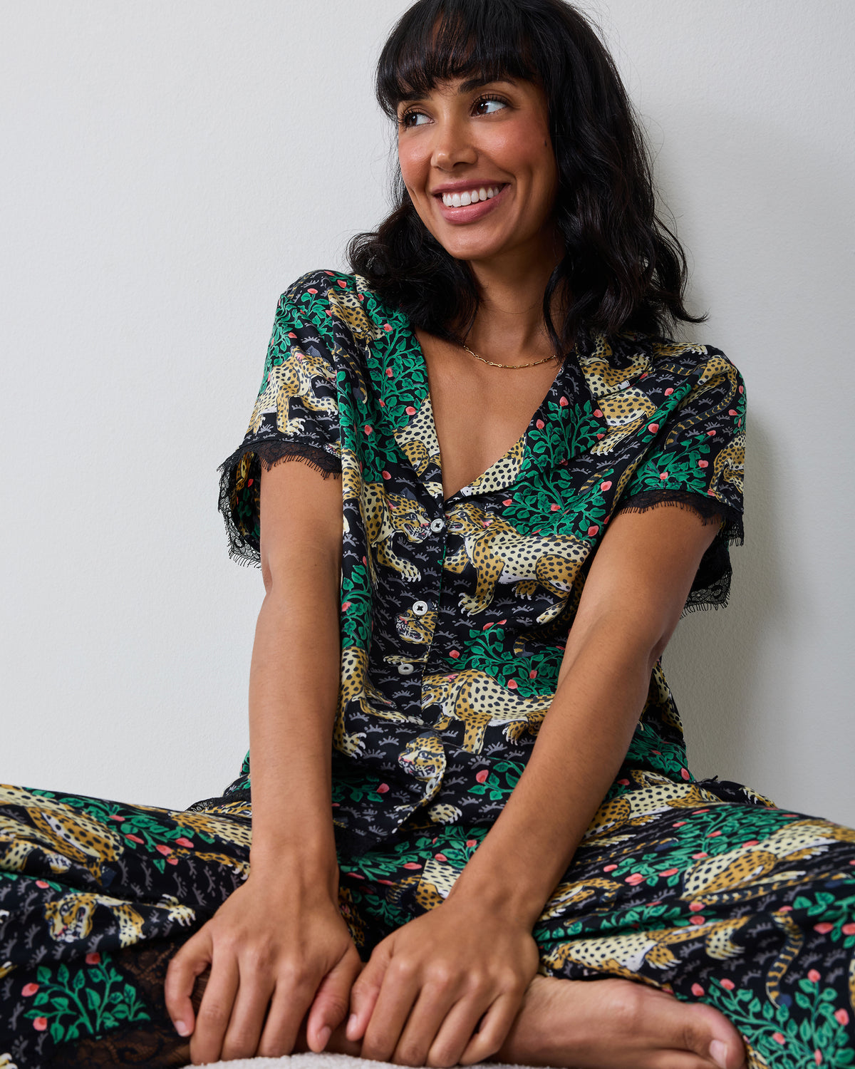 Model seated wearing the Bagheera Ink Jackie pajama set with a short-sleeve button-down top and lace-trimmed pants.