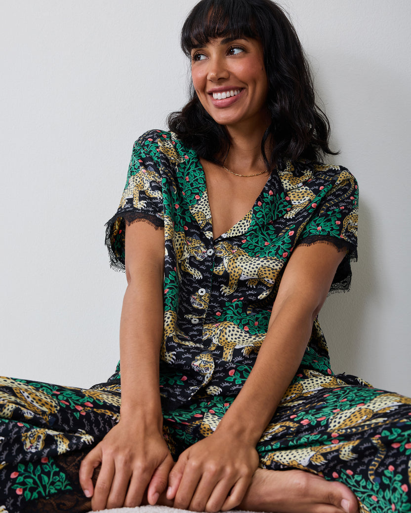 Model seated wearing the Bagheera Ink Jackie pajama set with a short-sleeve button-down top and lace-trimmed pants.