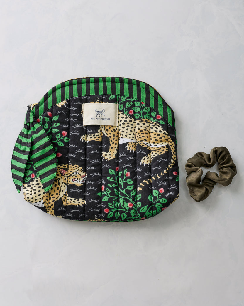 Bagheera Ink quilted makeup bag with leopard-and-leaf print, shown beside a brown scrunchie.