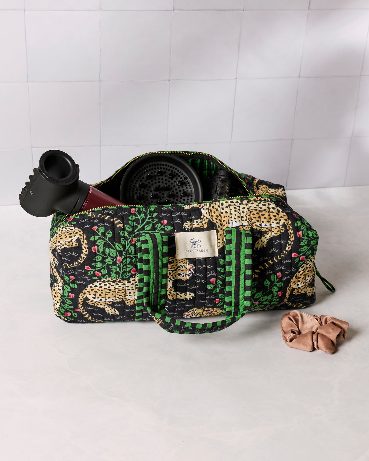 Black quilted zippered hair tool travel case with green trim and leopard-and-leaf print, shown open with hair styling tools inside.