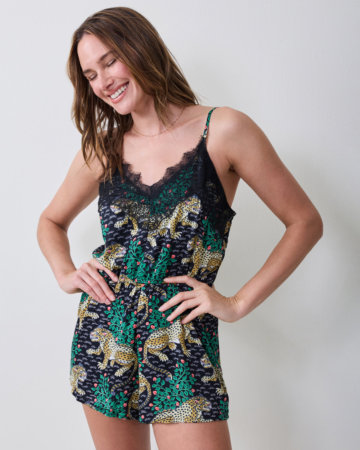 Close front view of the Bagheera Ink romper, showing its lace-trimmed neckline, thin straps, waist tie, and leopard-and-leaf print.