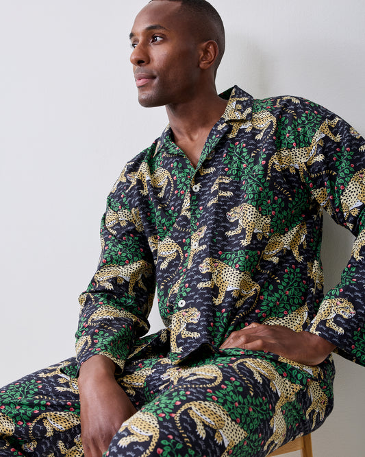 Person seated wearing a dark patterned button-front shirt and matching trousers with yellow spotted cats and green foliage.