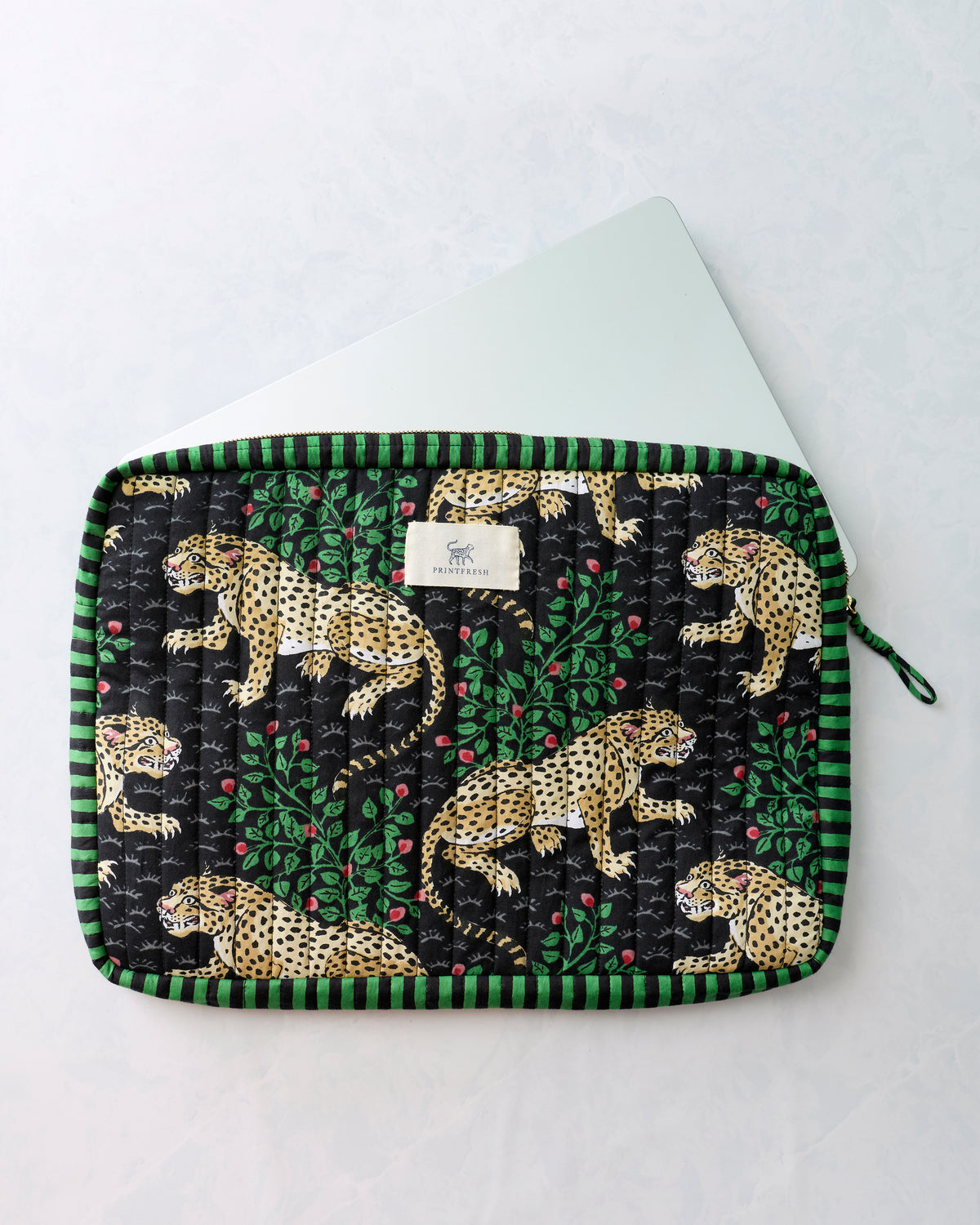 Black quilted leopard-print case with green striped edging, shown with the corner of a white laptop inside.